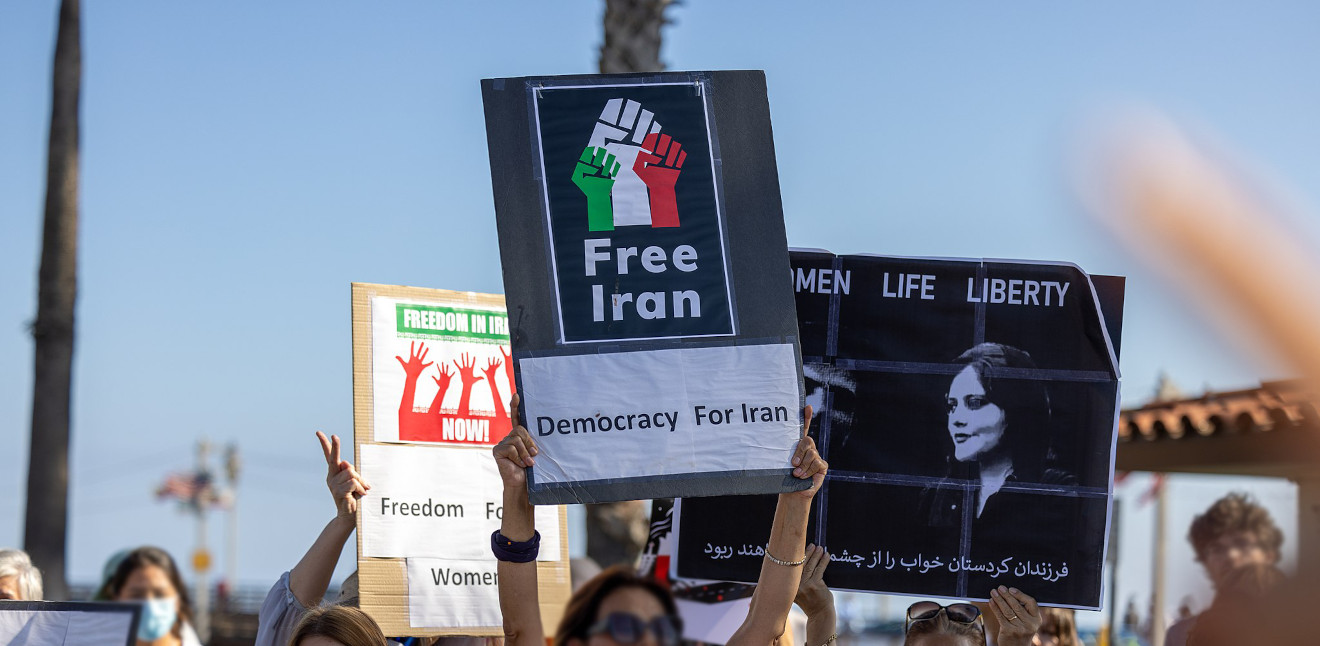 Eine Gruppe von protestierenden Frauen hebt Plakate in die Höhe. Sie tragen die Aufschriften 'Free Iran - Democracy for Iran' und 'Women - Life - Liberty' mit einem Porträt von Zhina Amini.